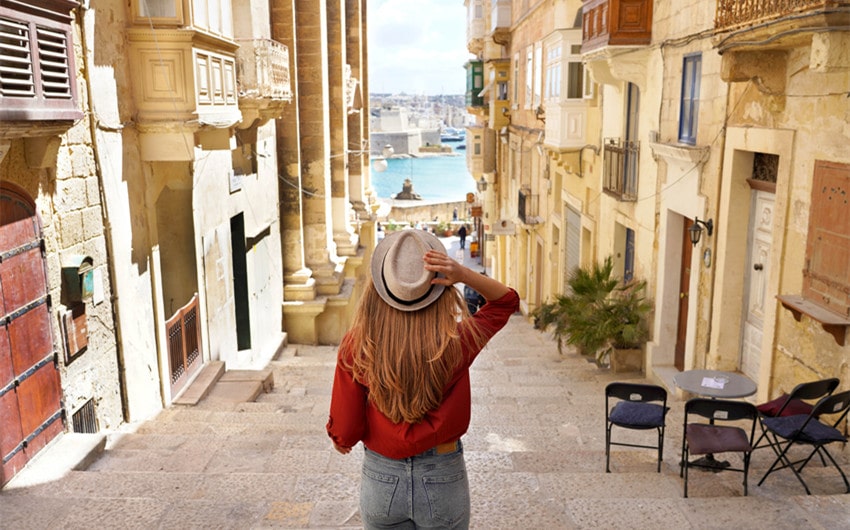 A woman looking at a quaint street. Her back is visible and she is wearing a hat.